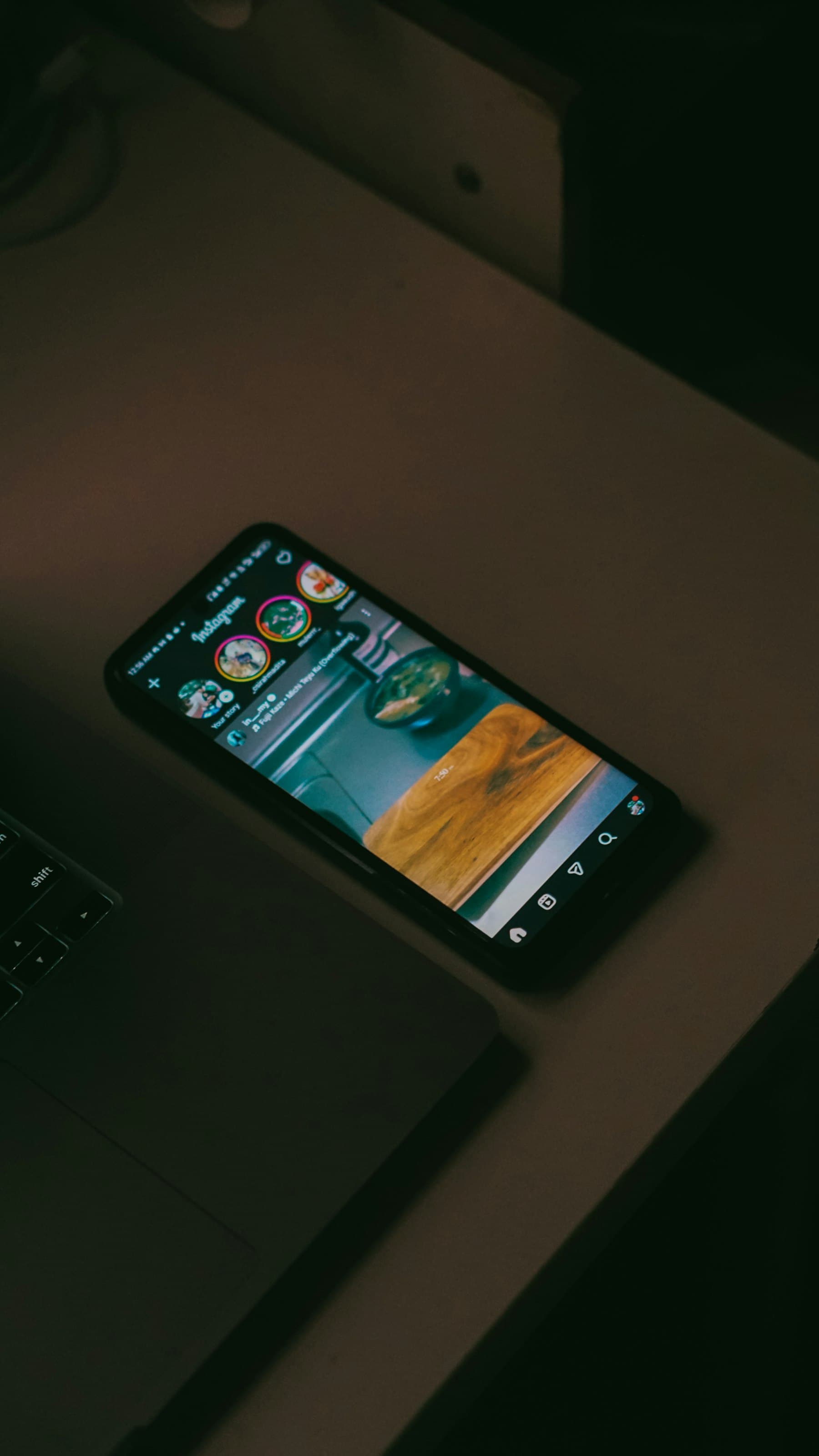 A phone on a desk, open to an Instagram feed, beside a laptop.